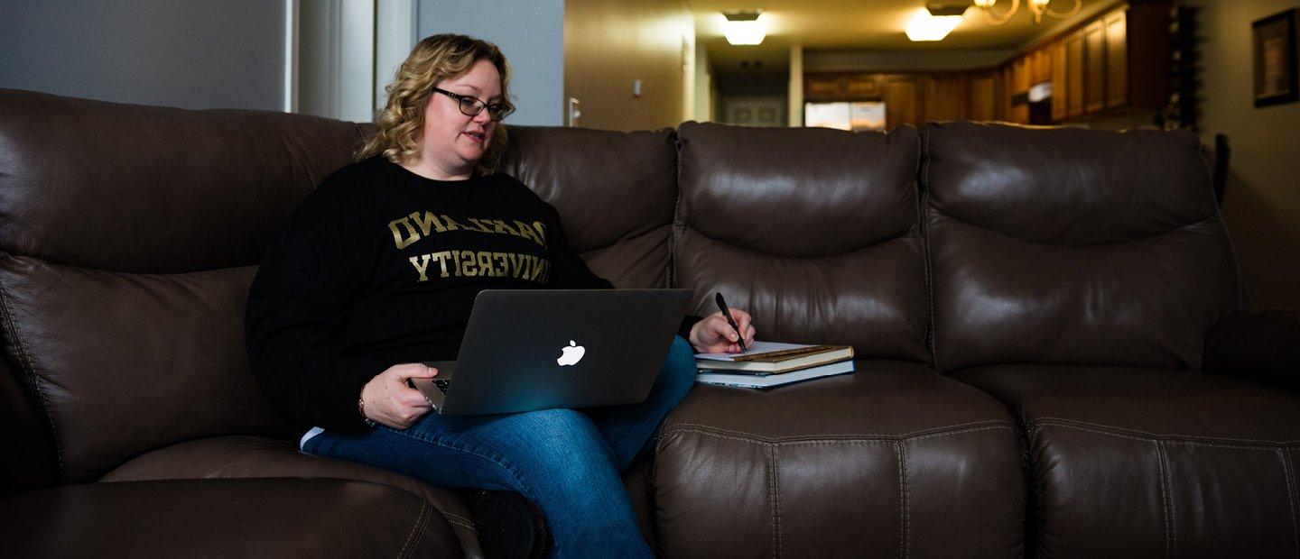 A woman sits on a living room sofa with her laptop open.